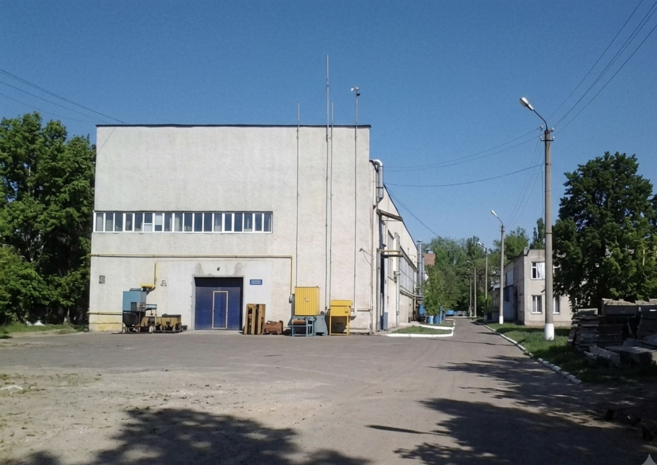 Внутрішній двір із заасфальтованим майданчиком, торець корпусу зі стрічковим склінням угорі та синіми воротами